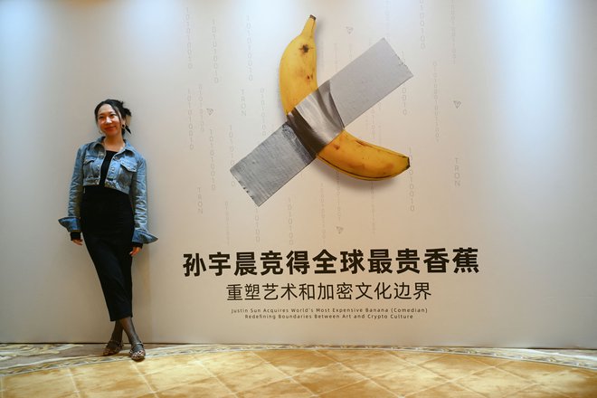 Ženska pozira za fotografijo pred plakatom, ki prikazuje umetniško delo banane, pred tiskovno konferenco Justina Suna v Hong Kongu. FOTO:  Peter Parks Afp