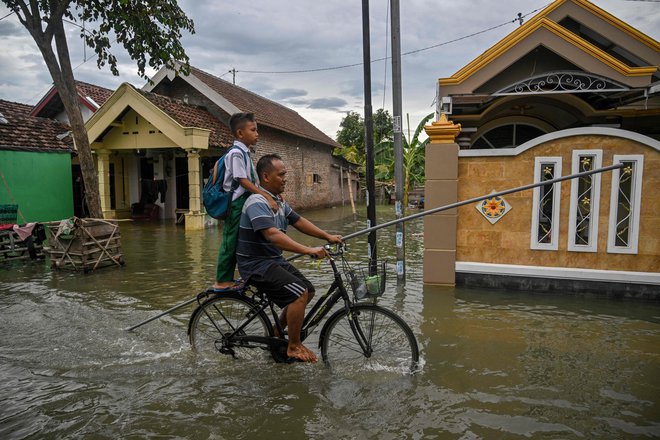 Moški in njegov sin se s kolesom prebijata skozi poplavljeno ulico v vasi Tempuran na Javi. Poplave na indonezijskem otoku je povzročilo večdnevno deževje. Foto: Juni Kriswanto/Afp