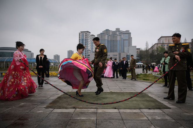 Poročni par skače čez vrv kot del običaja ob poroki. FOTO: Ed Jones/AFP