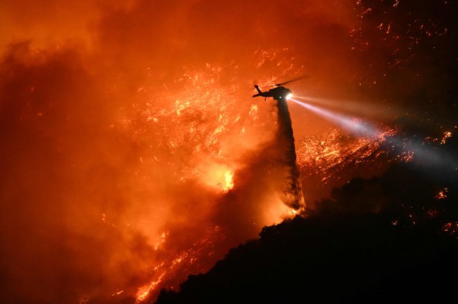 Gasilski helikopter spušča vodo nad zublji največja požara Palisades. FOTO: Patrick T. Fallon/AFP