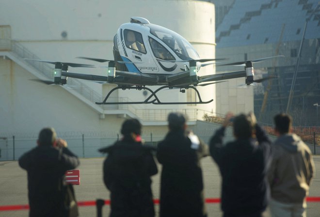 Ljudje opazujejo EH216-S, proizvodni model multicopterja z dvema potnikoma, ki ga je izdelalo podjetje Guangzhou EHang Intelligent Technology med njegovim prvim javnim poletom na heliportu v Šanghaju. Foto: Stringer/Afp