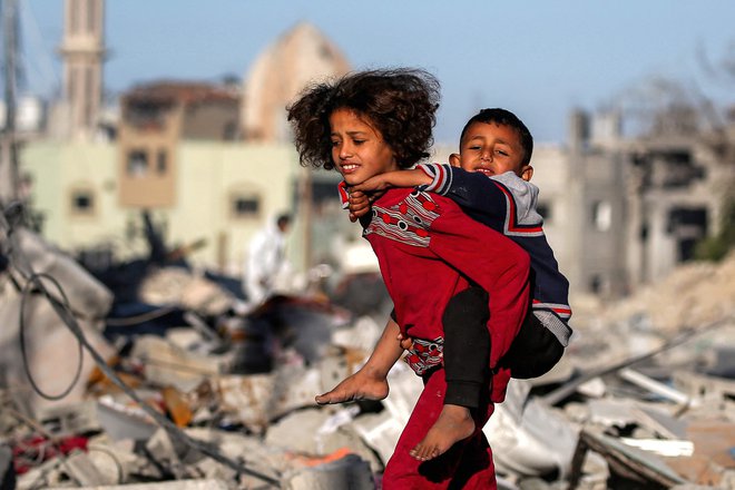 Deklica nosi dečka na hrbtu mimo ruševin  v Rafi na jugu Gaze, ko se prebivalci vračajo po dogovoru o prekinitvi ognja v vojni med Izraelom in Hamasom na palestinskem ozemlju. Foto: Eyad Baba/Afp