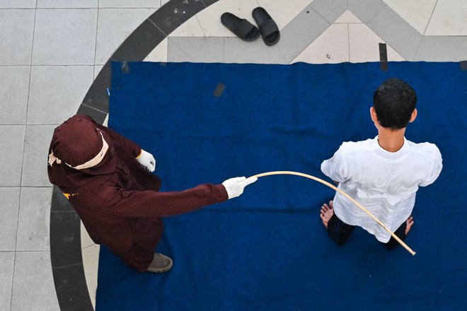 V Banda Acehu pripadnik šeriatske policije indonezijskega moškega z bičem kaznuje zaradi igranja spletnih iger na srečo. Foto: Chaideer Mahyuddin/Afp