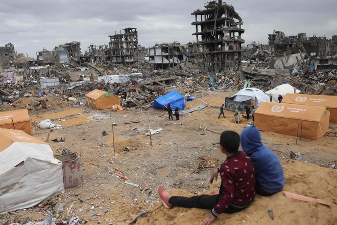 Razseljeni palestinski otroci sedijo na nasipu, ki gleda na šotore, postavljene med uničenimi stavbami v Džabaliji na severu območja Gaze. V začasnih zavetiščih, postavljenih v nekdanjih šolah, razstreljenih hišah in na pokopališčih po celotnem območju Gaze, ki ga je 15 mesecev uničevala vojna med Hamasom in Izraelom, več sto tisoč Palestincev nima niti plastične folije za zaščito pred zimskim dežjem in vetrom. Foto: Bashar Taleb/Afp