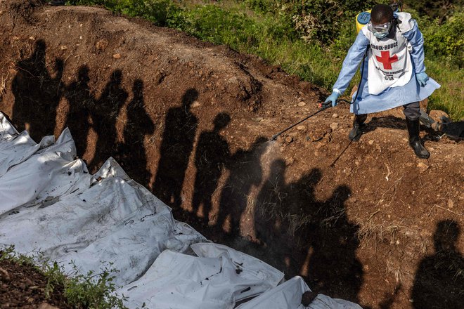 Sence prebivalcev, ki opazujejo člana kongovskega Rdečega križa, ki prši razkužilo na vreče s človeškimi ostanki na pokopališču v Bukavuju med množičnim pokopom žrtev spopadov na vzhodu DR Konga. Vojska je včeraj po lokalnih radijskih valovih pozvala vojake, ki bežijo v vzhodni provinci Severni Kivu, naj se ponovno pridružijo svojim enotam in nadaljujejo boj proti napredovanju upornikov M23. V mestu Lubero, proti kateremu napreduje skupina M23, 250 km severno od glavnega mesta province Goma, kongovski vojaki streljajo po mestu in plenijo. Foto: Luis Tato/Afp