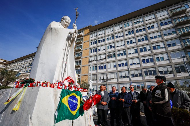 Ljudje se zbirajo pred bolnišnico in pred kipom nekdanjega papeža Janeza Pavla II. molijo za zdravje hudo bolnega 88-letnega papeža Frančiška. FOTO: Vincenzo Livieri/Reuters